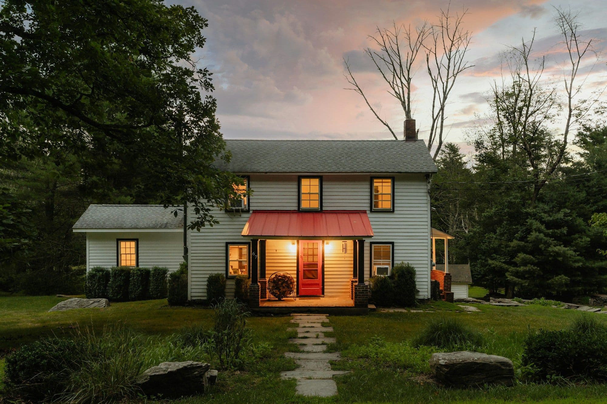 A small white house glowing at dusk, its porch lights on