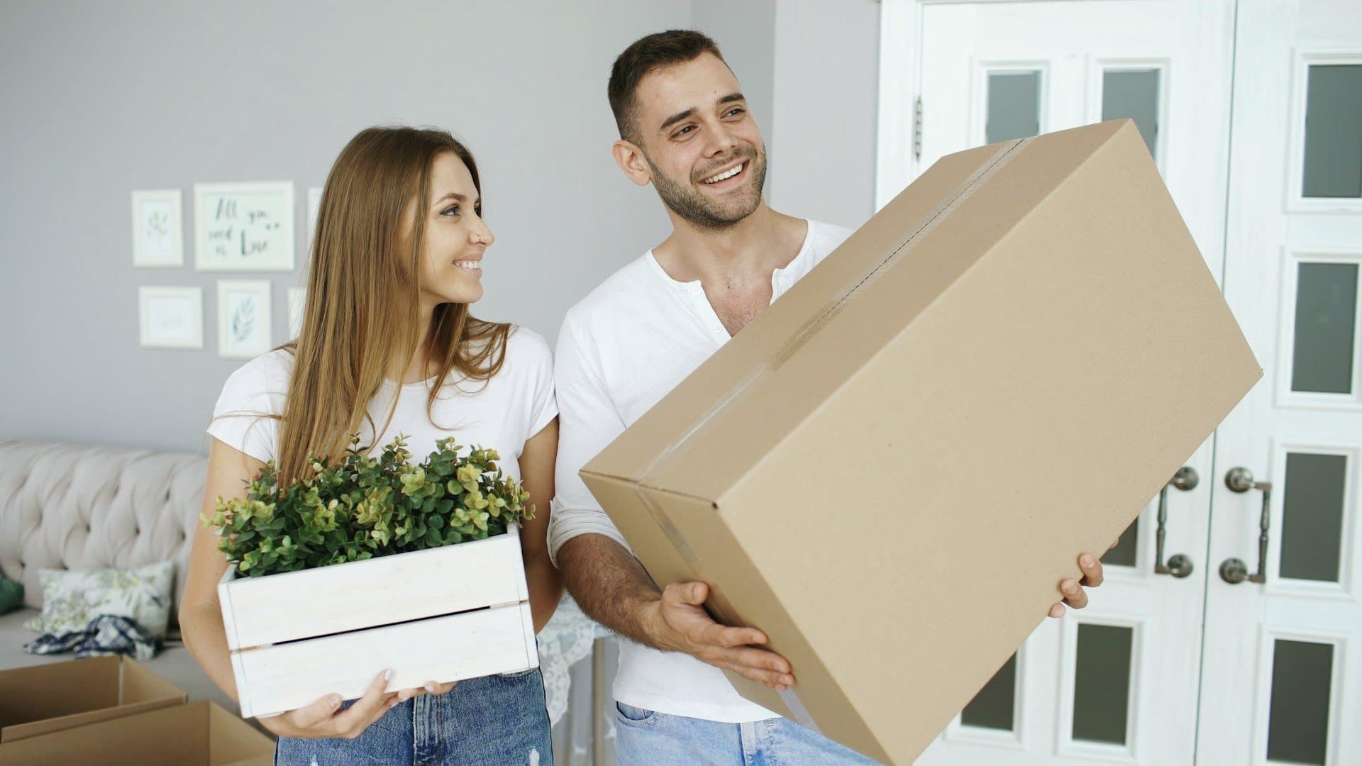 A couple smiling as they carry their first boxes into a new home