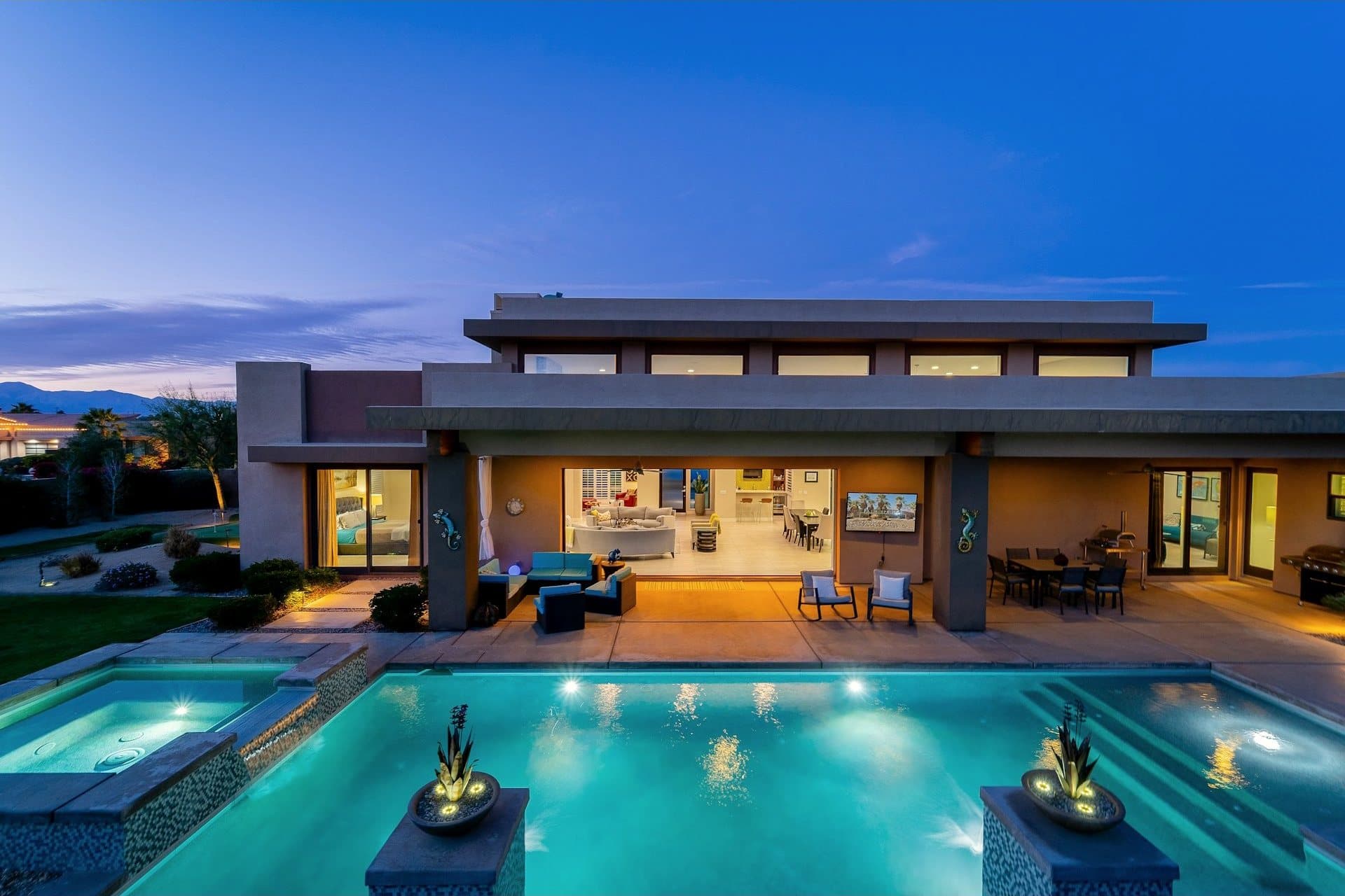 A contemporary home with a lit pool and outdoor living at twilight